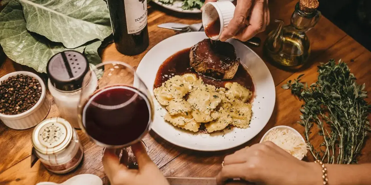Elegancka kolacja z ravioli i wołowiną w sosie. Idealne pytanie: jakie wino do gotowania? Czerwone wino i świeże zioła dopełniają atmosferę.