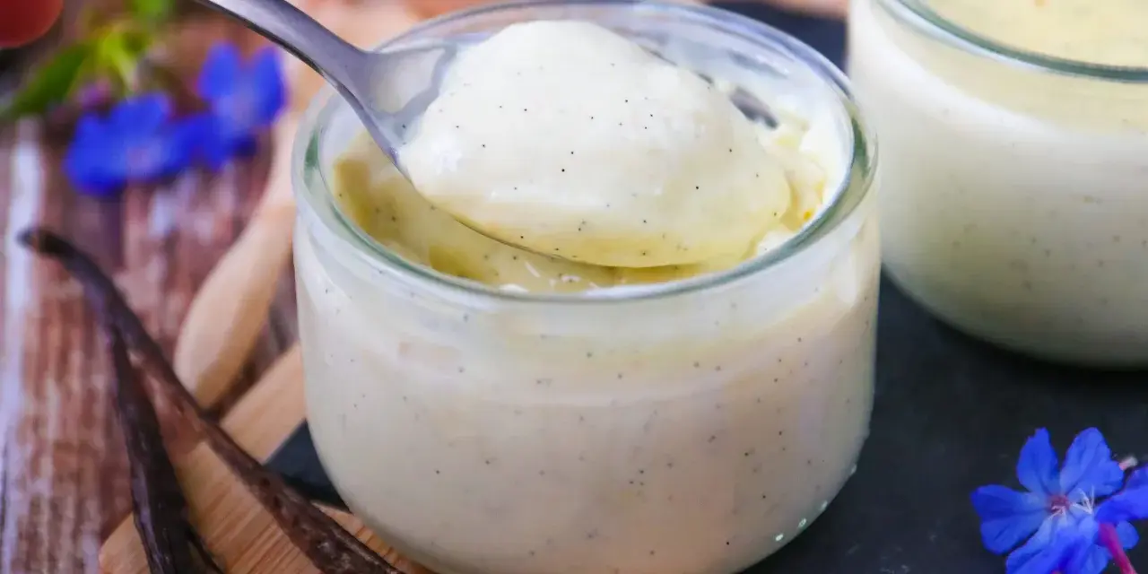 Délicieuse crème vanille recette, onctueuse et parsemée de grains de vanille, servie dans un pot en verre.