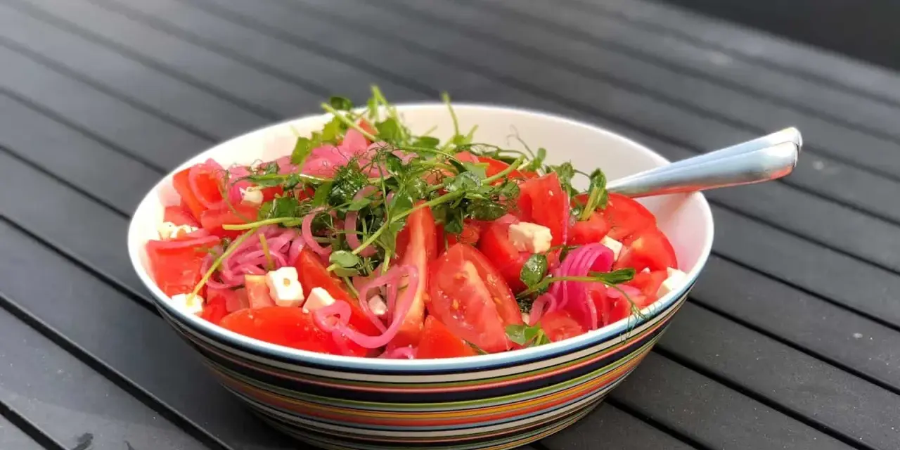 Enkel sallad med tomater, fetaost, rödlök och groddar i en färgglad skål.