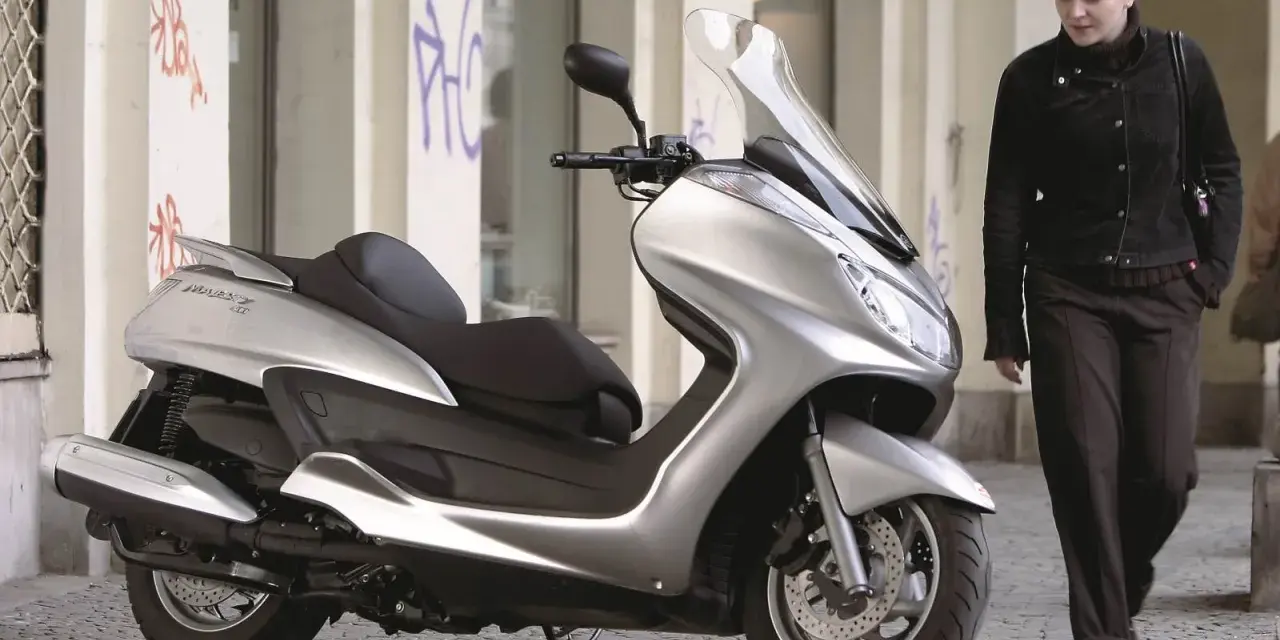 Srebrny skuter Yamaha Majesty 400, symbol miejskiej elegancji, obok kobiety w ciemnej kurtce.