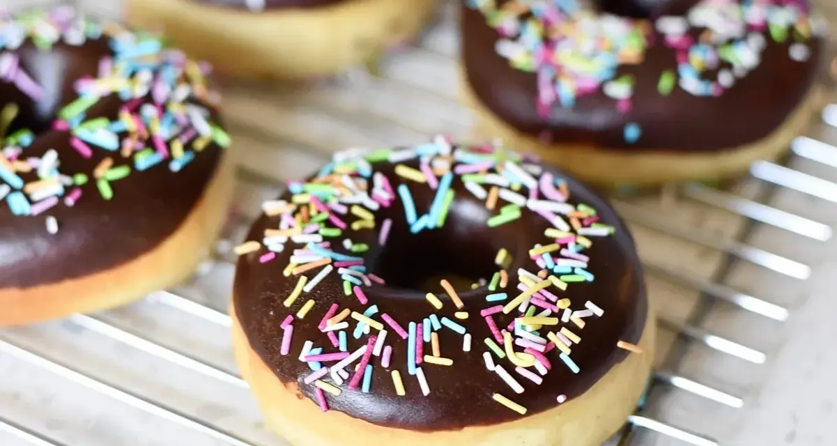 Färska, hembakade donuts med chokladglasyr och färgglatt strössel ligger på ett galler. Perfekt för att baka donuts!