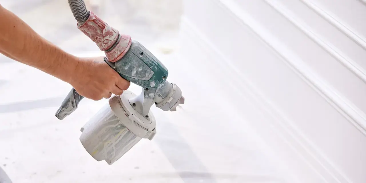Mano che tiene una pistola a spruzzo per verniciare un cancello bianco, creando un effetto liscio e uniforme.