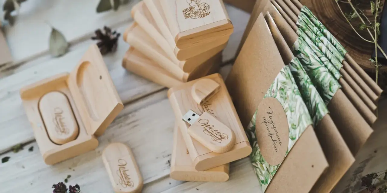 Drewniane pendrive'y z grawerem "Wedding" i koperty z motywem roślinnym. Personalizowane upominki dla gości od pary młodej to klucz do sukcesu.