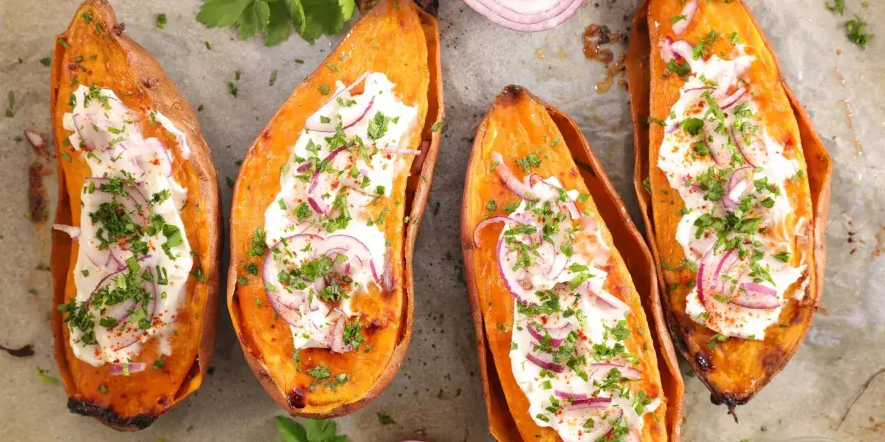 Quatre moitiés de patate douce au four, garnies de crème, oignons rouges et persil. Un délice simple et savoureux.