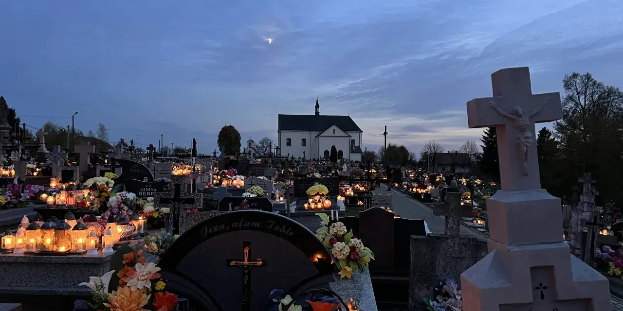 Cmentarz nocą, pełen płonących zniczy i kwiatów. W oddali kościół, a na niebie księżyc. Modlitwa świętej Gertrudy w ciszy zadumy.