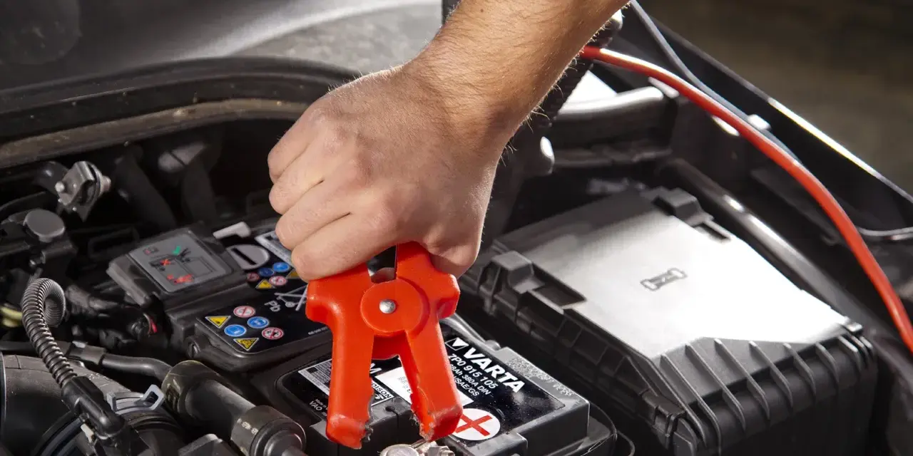 Starthilfe: Rote Klemme am Pluspol, warum nicht minus an minus? Ein Mann klemmt ein Starthilfekabel an die Autobatterie.
