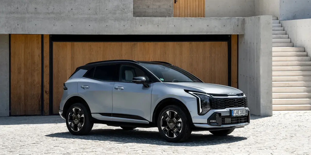 Elegancki, srebrny Kia Sportage Hybrid na tle nowoczesnej architektury z drewnianymi drzwiami i betonowymi schodami.