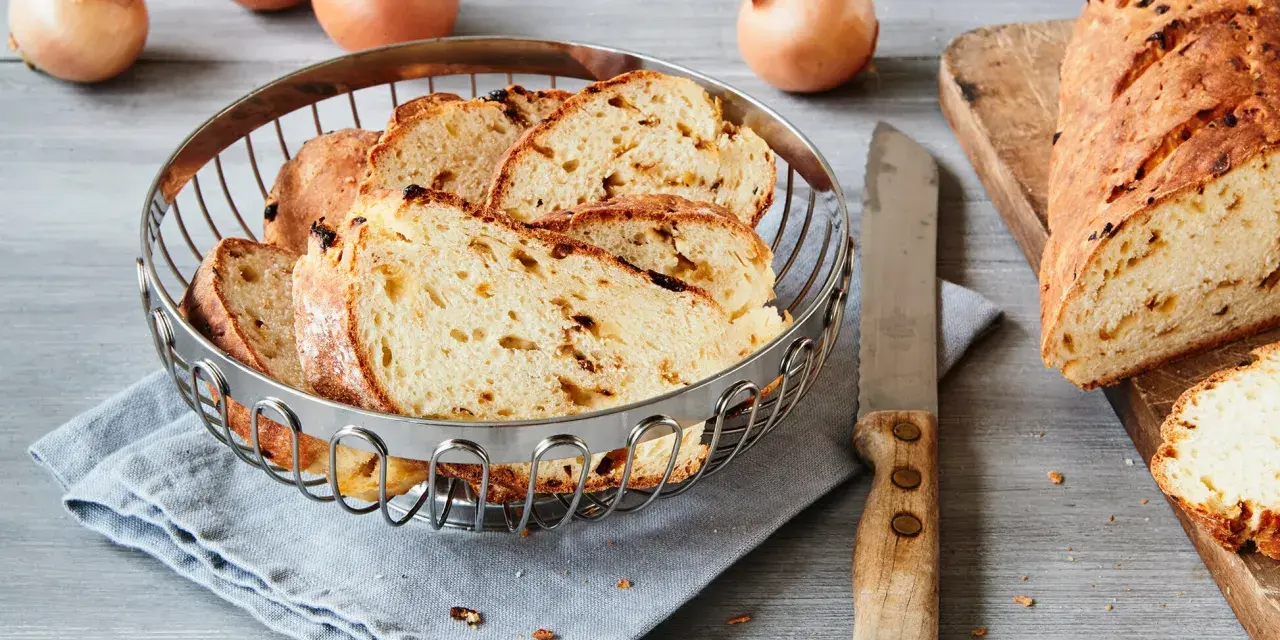 Frisch gebackenes Zwiebelbrot, bereit für ein leckeres Zwiebelbrot Rezept. Ganze Zwiebeln liegen daneben.