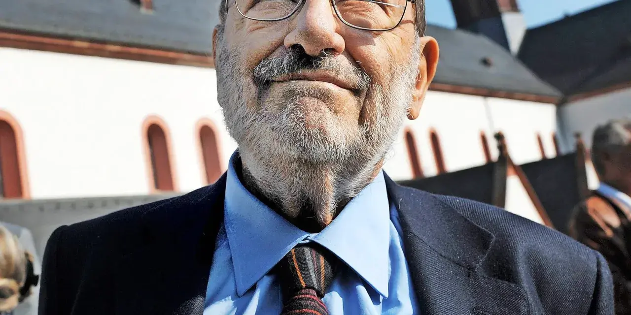 Porträt eines älteren Mannes mit Brille, Schnurrbart und Bart, der einen Anzug und eine Krawatte trägt.