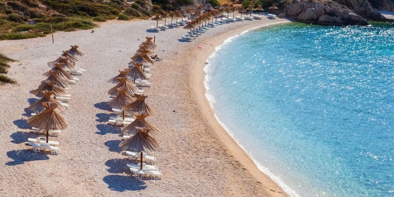 Rządki parasoli i leżaków na kamienistej plaży, obok krystalicznie czystej, turkusowej wody. To jedna z najpiękniejszych plaż w Europie.
