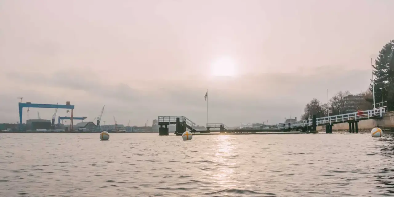 Kiel im Winter: Hafenkräne und eine Mole im nebligen Licht. Bojen treiben auf dem ruhigen Wasser.