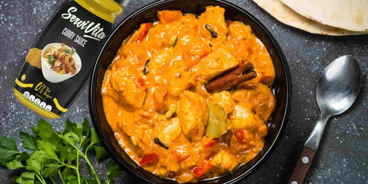Bol de pollo al curry cremoso con especias, salsa y pan naan al lado.