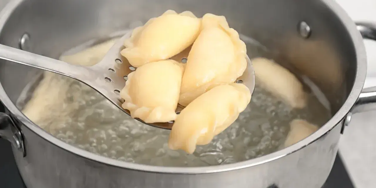 Pierogi gotujące się w garnku, wyjmowane łyżką cedzakową.