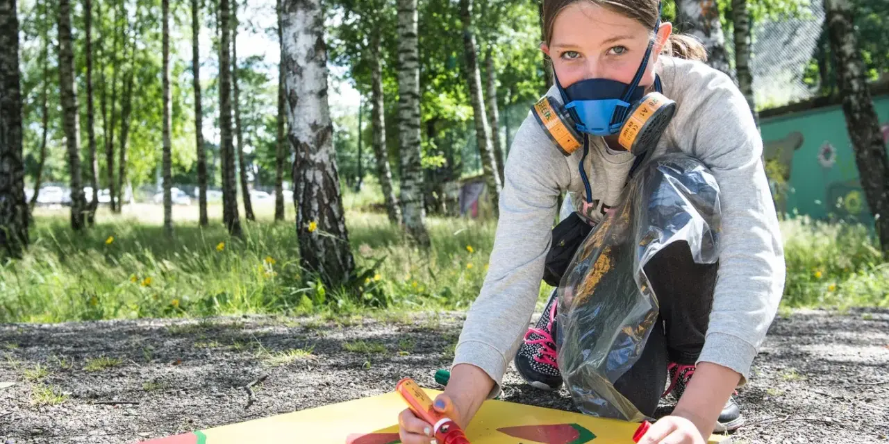 Ung flicka med munskydd skapar graffiti på papper utomhus.