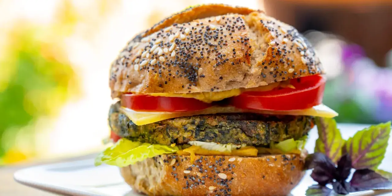 Deliciosa hamburguesa de espinacas con pan de semillas, queso, tomate y lechuga, servida en un plato blanco.