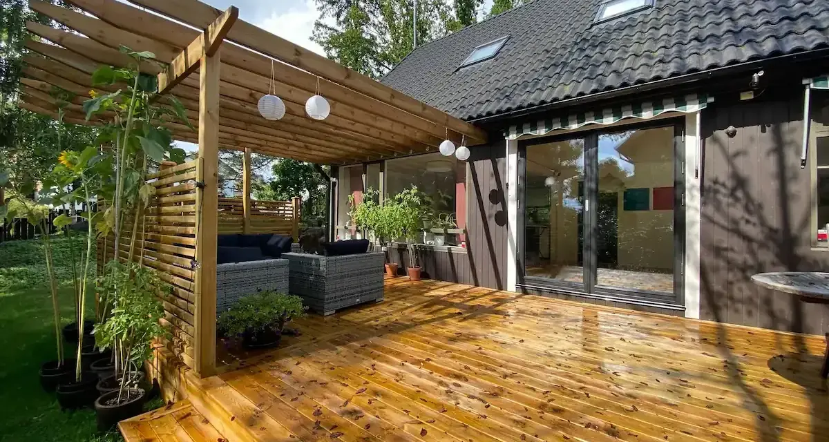 Trall med synliga skruvar kan vara en nackdel för utseendet. Här en altan med pergola, utemöbler och solrosor.