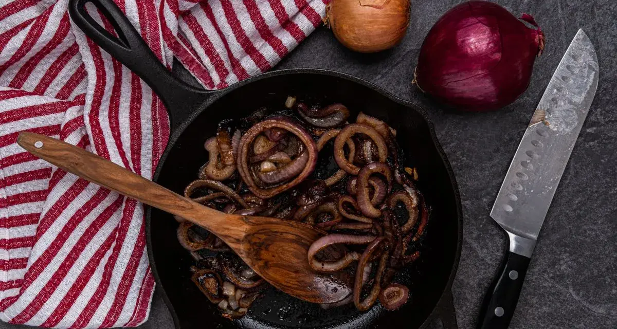 Cipolle in agrodolce caramellate in padella, pronte per essere gustate. Accanto, cipolle fresche e un coltello affilato.