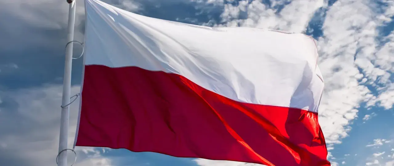 Flaga biało-czerwona powiewa na wietrze na tle błękitnego nieba z chmurami.