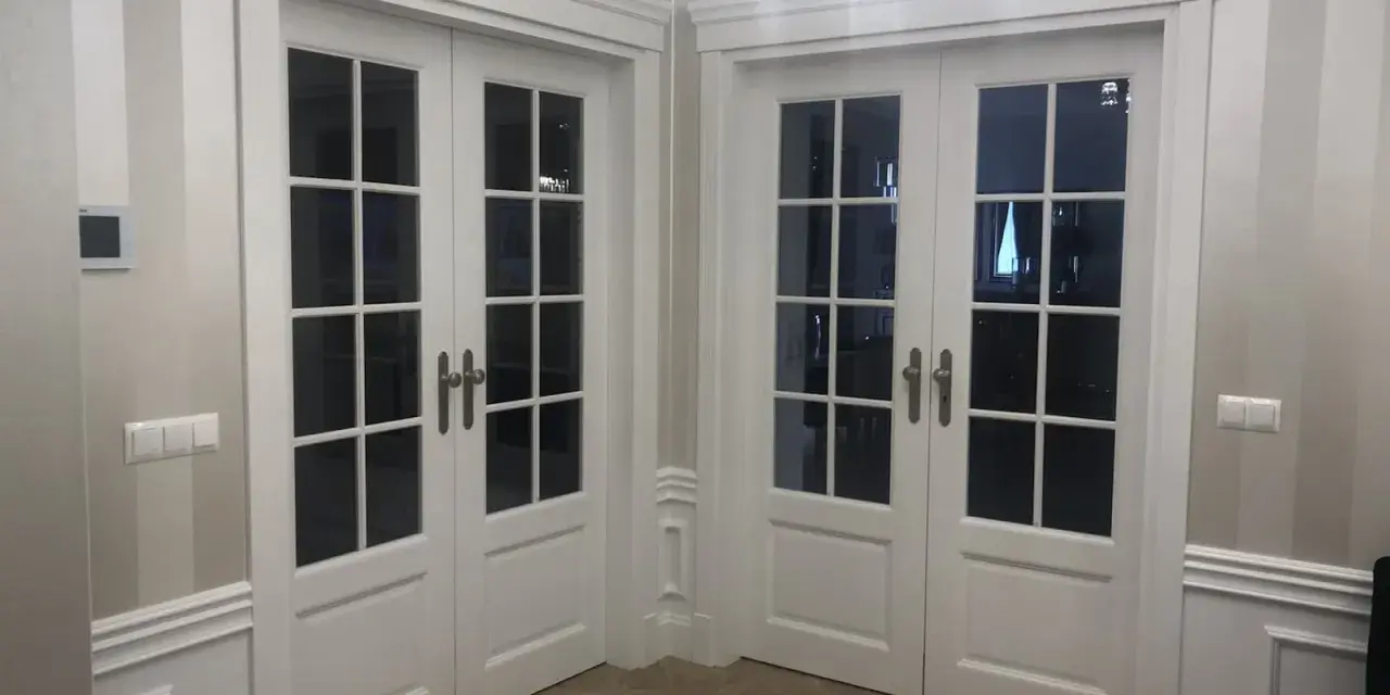 Eleganckie białe drzwi dwuskrzydłowe z przeszkleniem, osadzone w metalowych futrynach, tworzą stylowe przejście.