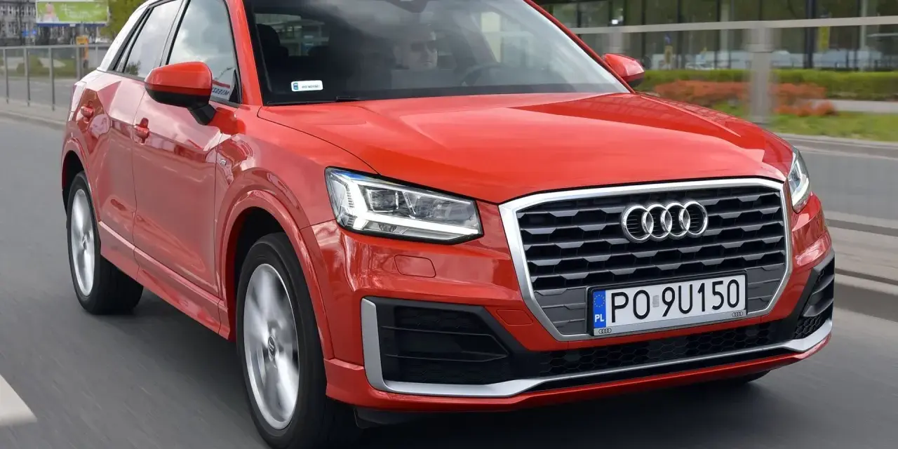 Czerwone Audi Q2 w ruchu miejskim. Choć jego design jest atrakcyjny, warto rozważyć potencjalne wady, takie jak ograniczona przestrzeń bagażowa.