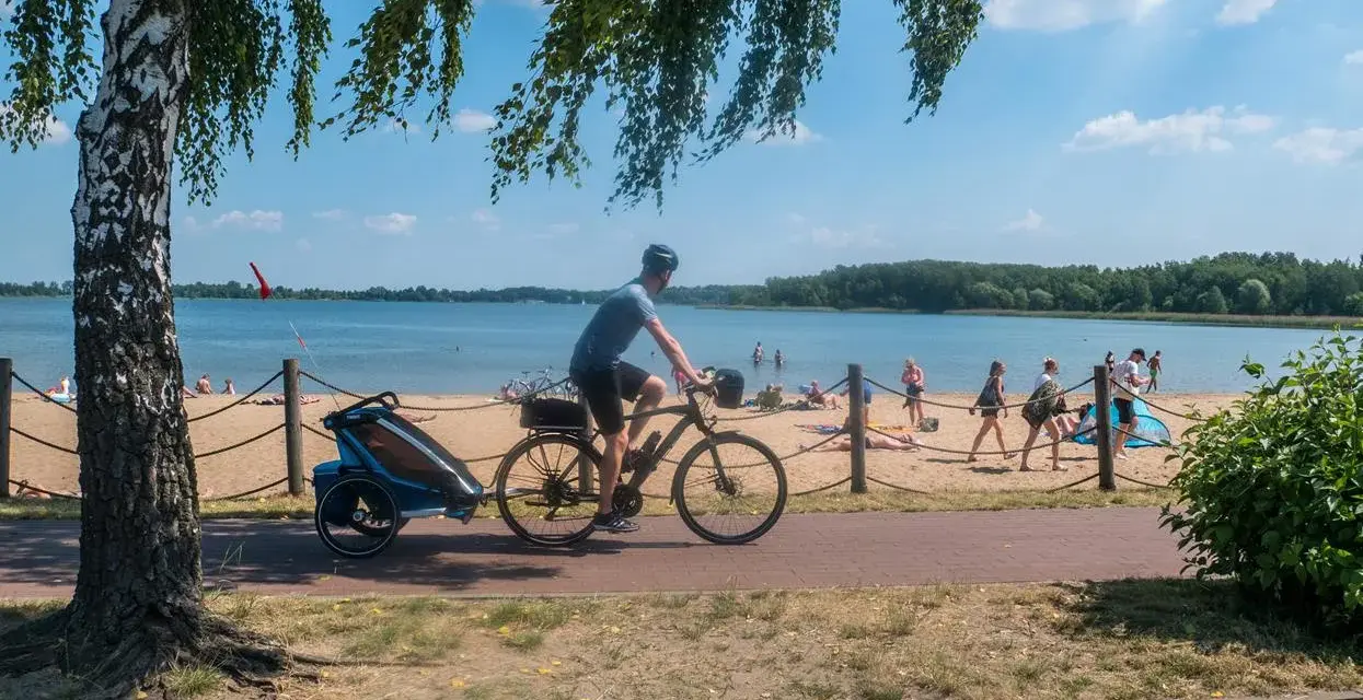 Mężczyzna na rowerze z przyczepką jedzie ścieżką rowerową wzdłuż plaży. To idealne miejsce na wycieczkę trasą pogoria 3.