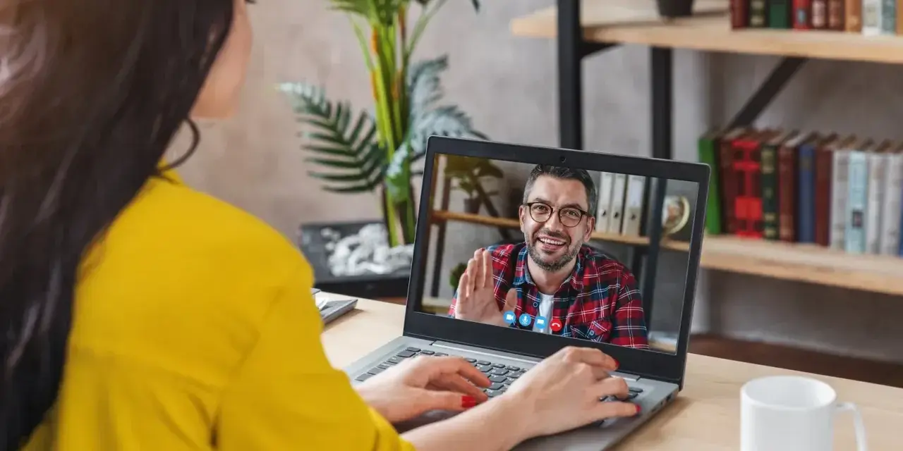 Kobieta na wideo rozmowie z mężczyzną, który uśmiecha się i macha. Może to być konsultacja online, np. test na autyzm.