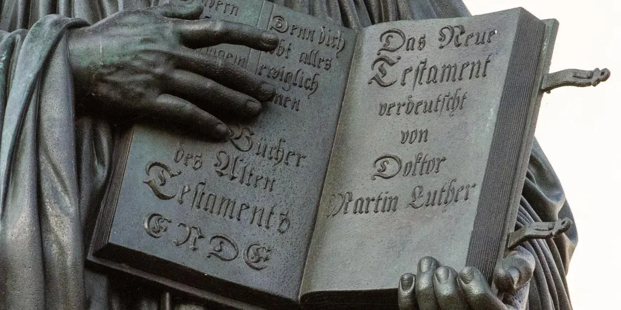 Hände halten ein aufgeschlagenes Buch mit Luthers Übersetzung des Neuen Testaments. Die Bedeutung der Reformation wird durch diese Darstellung greifbar.