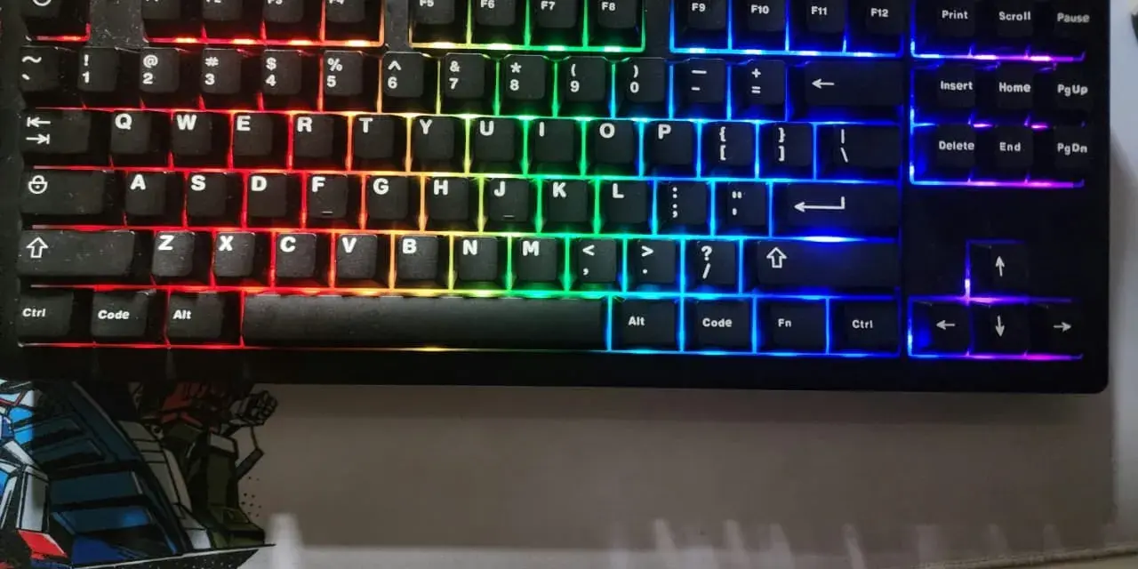 Eine schwarze Tastatur mit bunter RGB-Beleuchtung, die wie ein Regenbogen verstellt ist. Die Tasten leuchten in Rot, Orange, Gelb, Grün, Blau und Violett.
