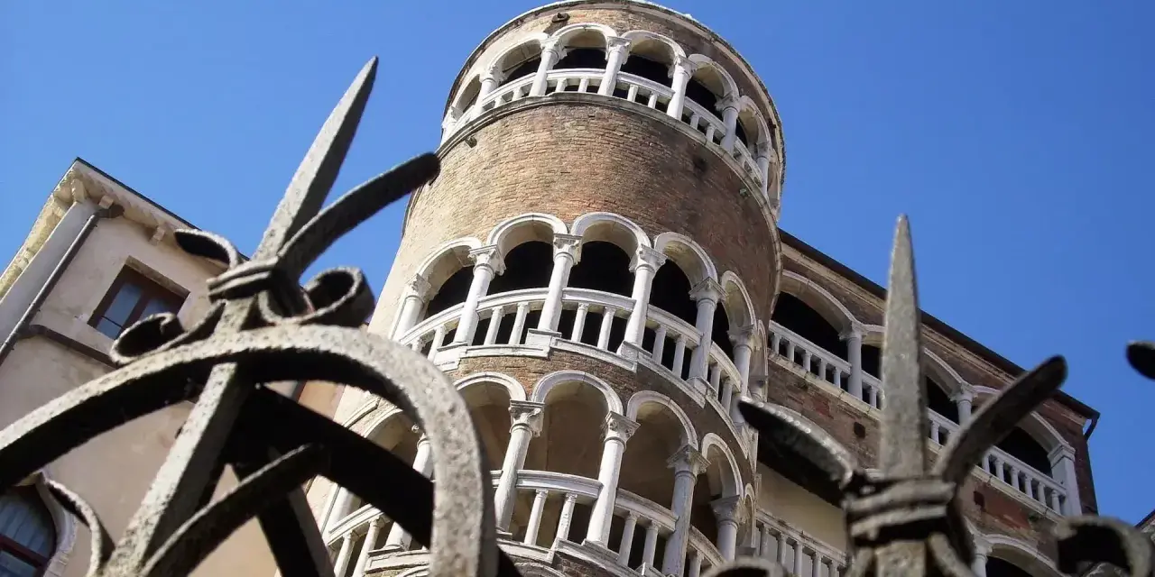 La Torre del Bovolo, con la sua architettura a chiocciola e i suoi loggiati, si staglia contro il cielo azzurro, vista attraverso un cancello in ferro battuto.