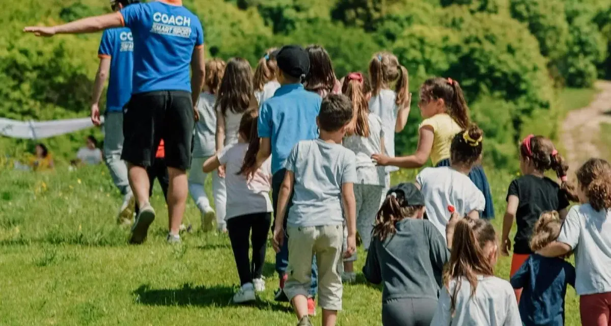 Un groupe d'enfants suit un coach sur une colline verdoyante. Ces actions pour financer un voyage scolaire sont pleines d'énergie et de joie.