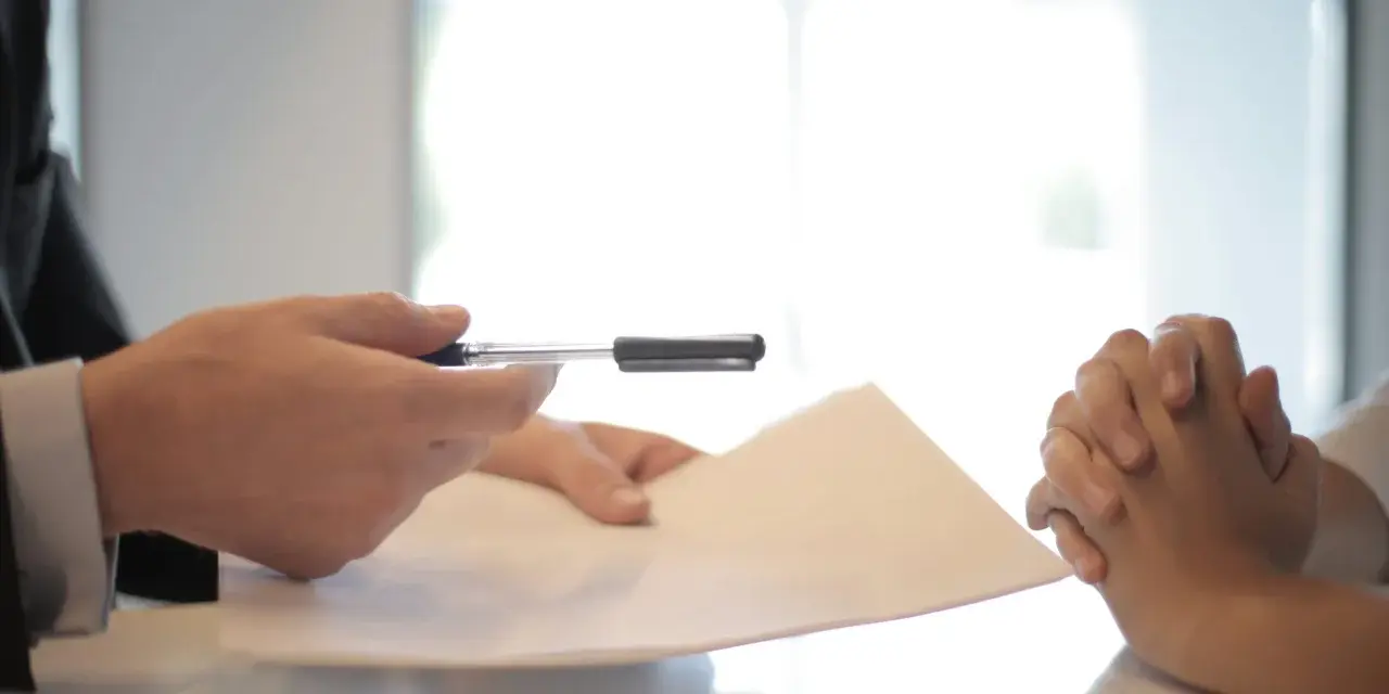Man en traje entrega documento a persona con manos entrelazadas, discutiendo cómo devolver fianza alquiler antes finalizar contrato.