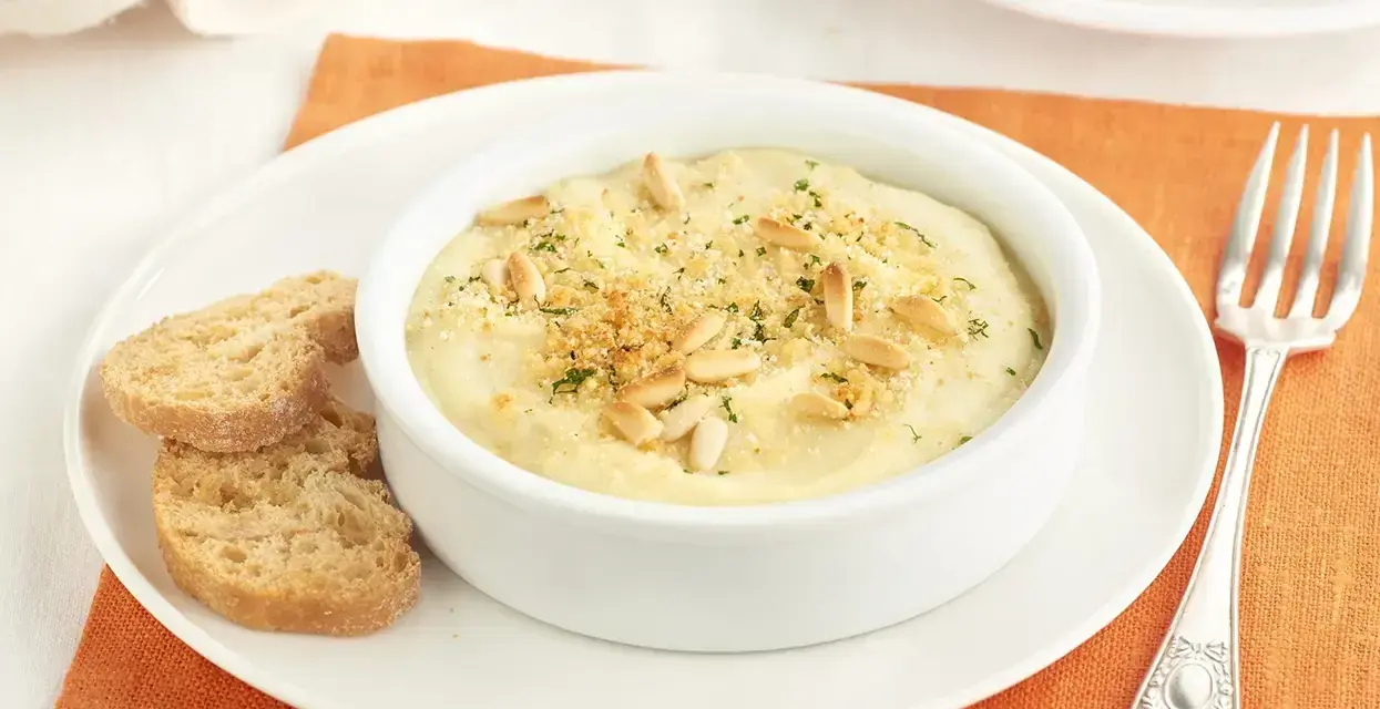 Deliciosa brandada de merluza cremosa, gratinada con piñones y pan rallado, servida con tostas.