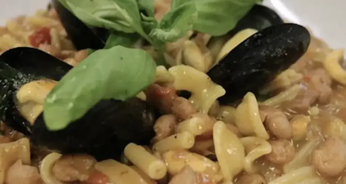Un piatto invitante di pasta fagioli e cozze, guarnito con foglie di basilico fresco.