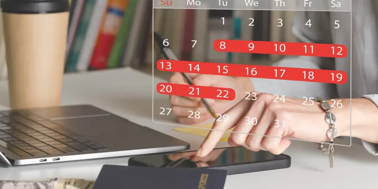 Planowanie urlopu zgodnie z kodeksem pracy. Na biurku laptop, paszport, pieniądze i kalendarz z zaznaczonymi dniami.