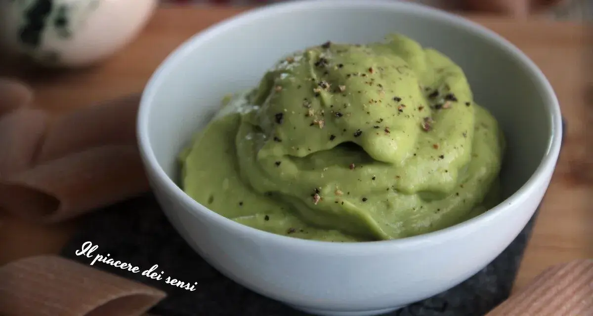 Una ciotola bianca piena di vellutata crema di avocado, cosparsa di pepe nero macinato. Accanto, pasta integrale.