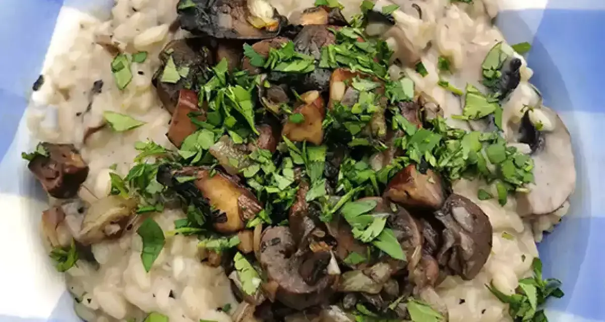 Risotto cremoso con champiñones salteados y perejil picado en un plato azul a cuadros.