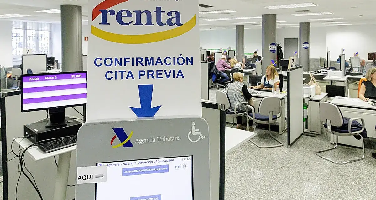 Oficina de la Agencia Tributaria con gente esperando. Un cartel indica "Confirmación cita previa" y una pantalla táctil para gestionar citas, resolviendo la duda de cuanto tarda Hacienda en cobrar la renta.