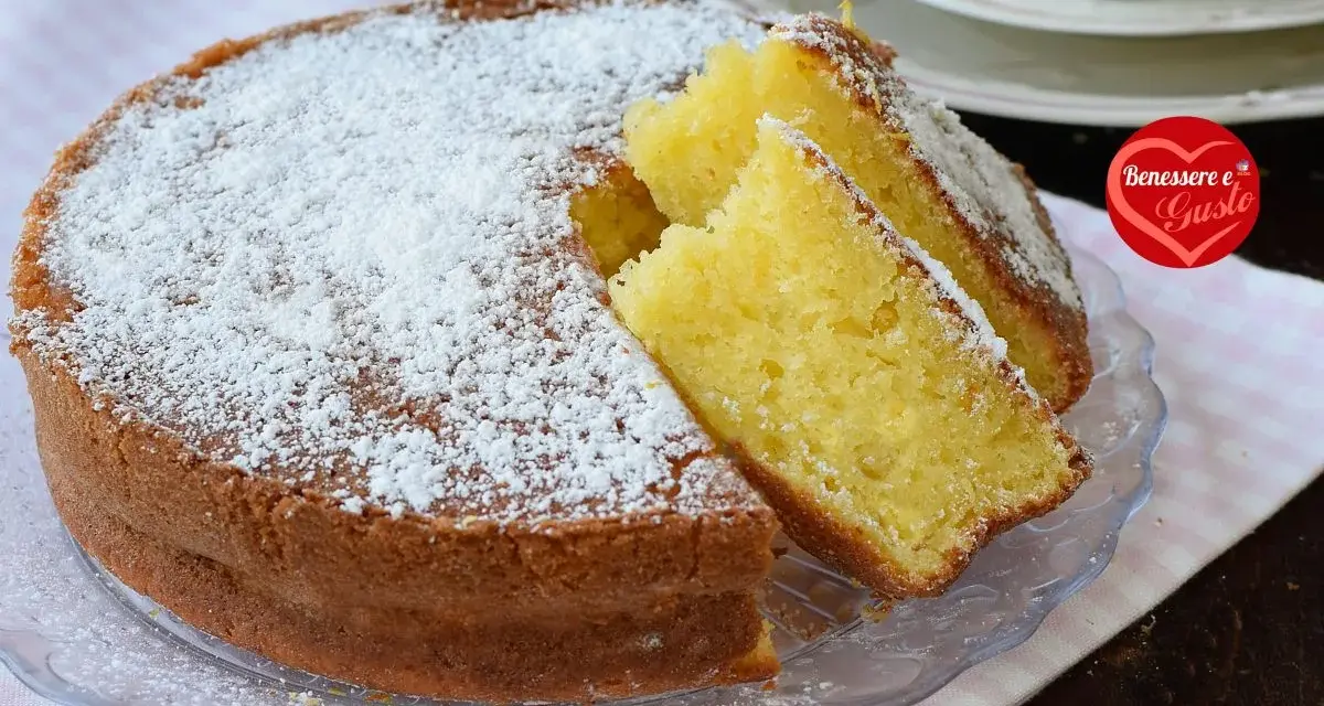 Una soffice torta allo yogurt, cosparsa di zucchero a velo, con due fette tagliate per mostrare la sua morbidezza. Perfetta per la colazione o la merenda.