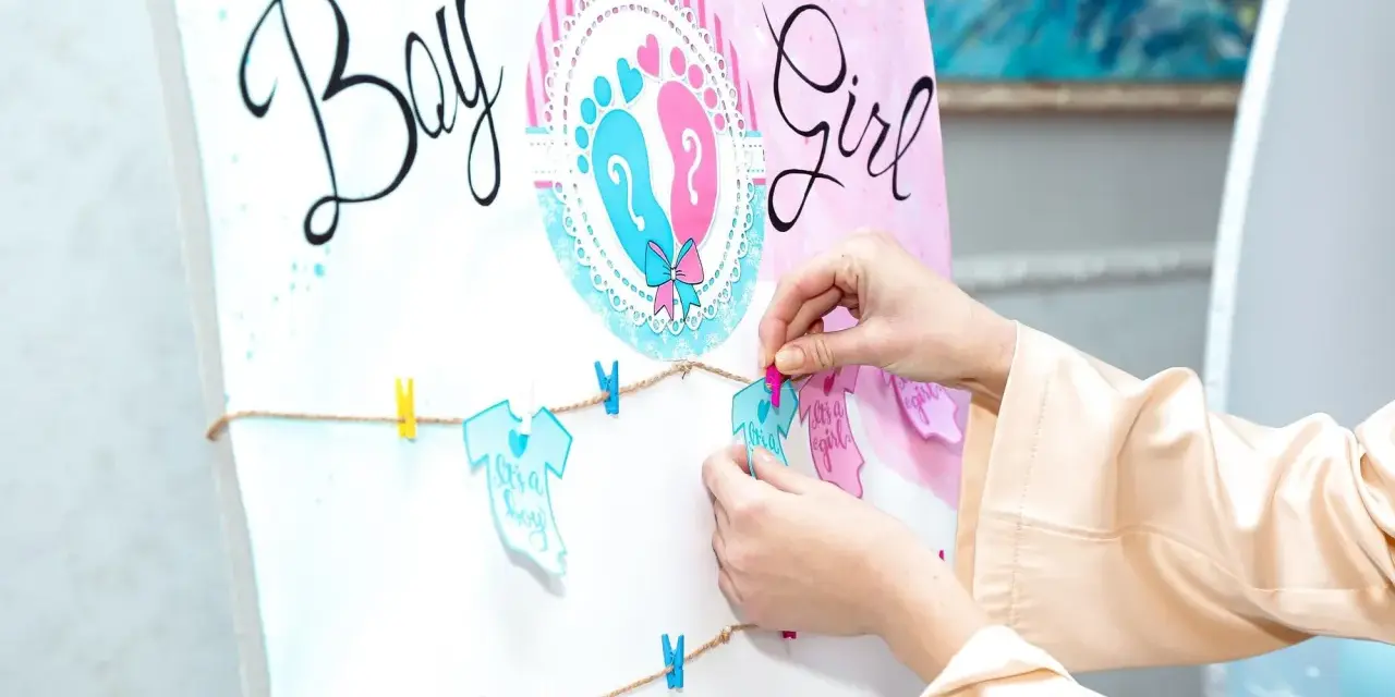 Ręce wieszają ozdoby na przyjęciu z okazji baby shower, kiedy płeć dziecka jest pewna. Napisy "Boy" i "Girl" oraz dziecięce ubranka.