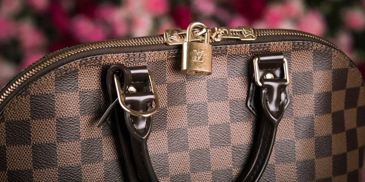 Dettaglio di una borsa Louis Vuitton, icona dell'azienda, con il classico motivo a scacchiera e un lucchetto dorato.