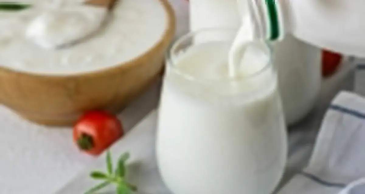 Ayran co to? Orzeźwiający napój mleczny, idealny na upalne dni, nalewany do szklanki. Obok miska z jogurtem i pomidorek.
