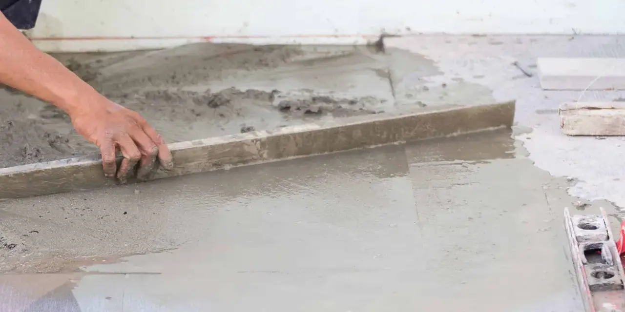 Ręka wyrównuje świeży beton, tworząc idealnie gładką podłogę na gruncie.