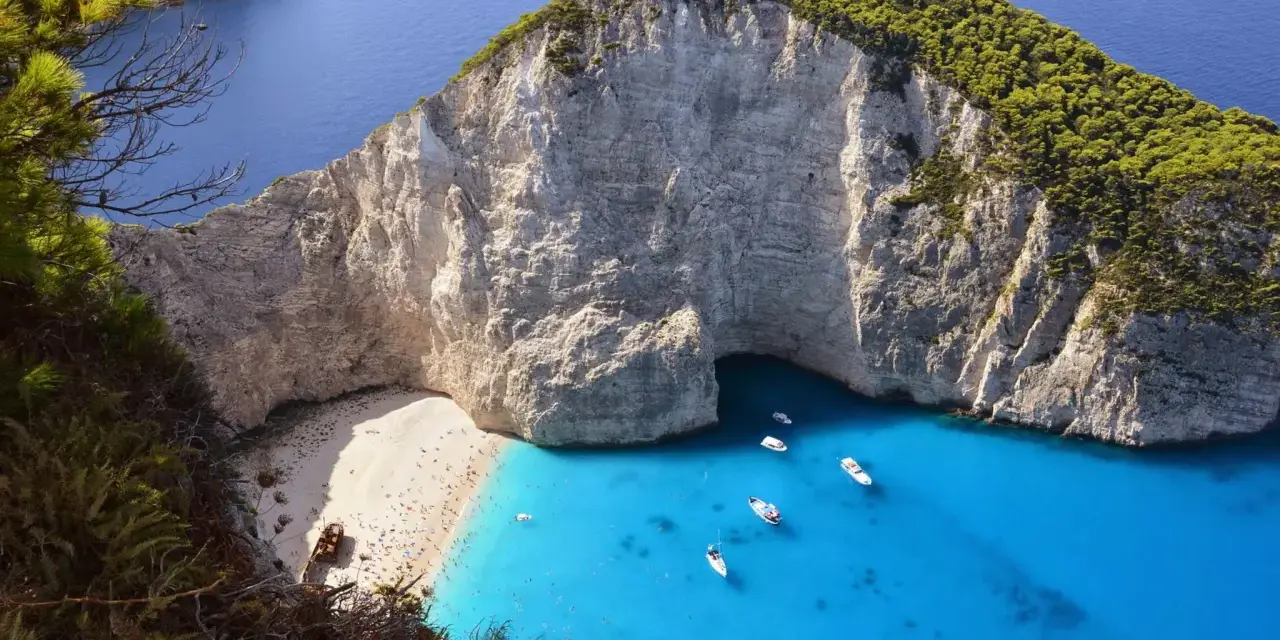 Widok na zatokę Navagio na Zakynthos z plażą, turkusową wodą i łodziami.