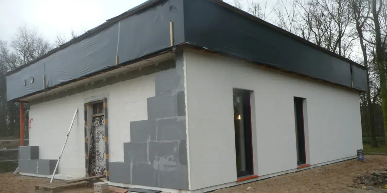 Budowa domu ze styropianu w trakcie. Widoczne bloczki, okna i dach przykryty czarną folią.