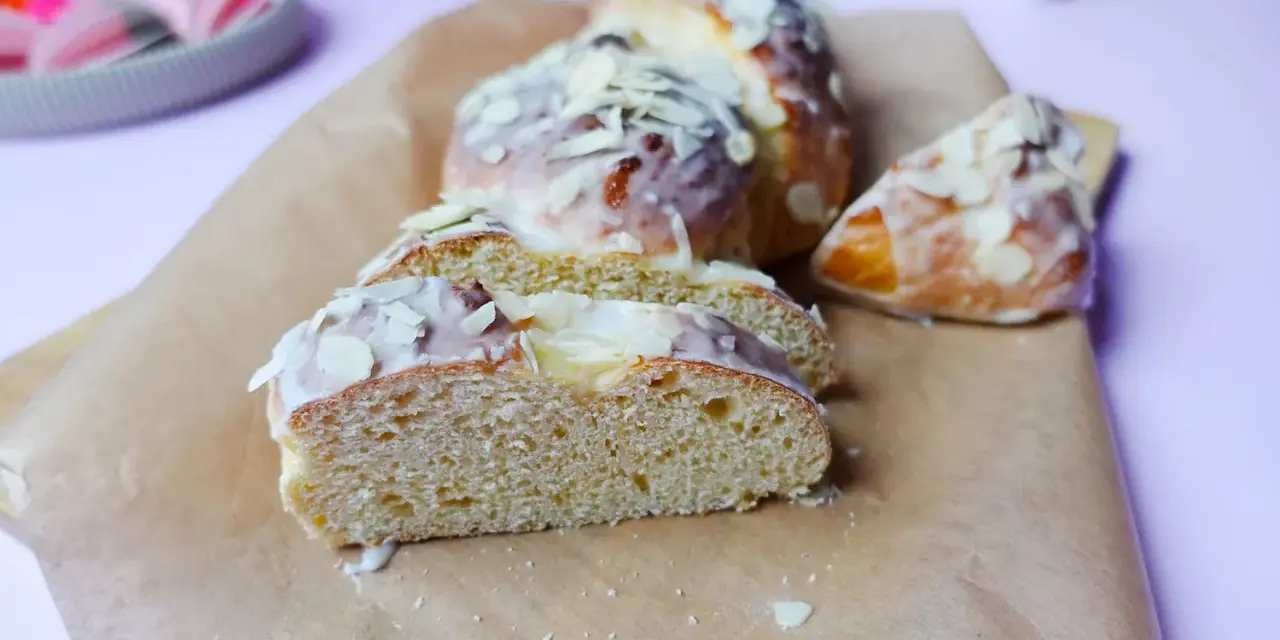 Süßer Hefekuchen ohne Zucker, mit zarter Glasur und Mandelblättchen bestreut, auf Backpapier angerichtet.