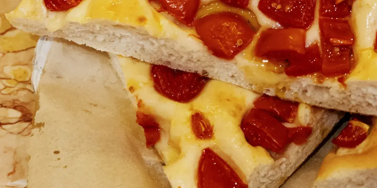Saftige Focaccia Pomodoro mit geschmolzenem Käse und sonnengetrockneten Tomaten, auf Backpapier serviert.