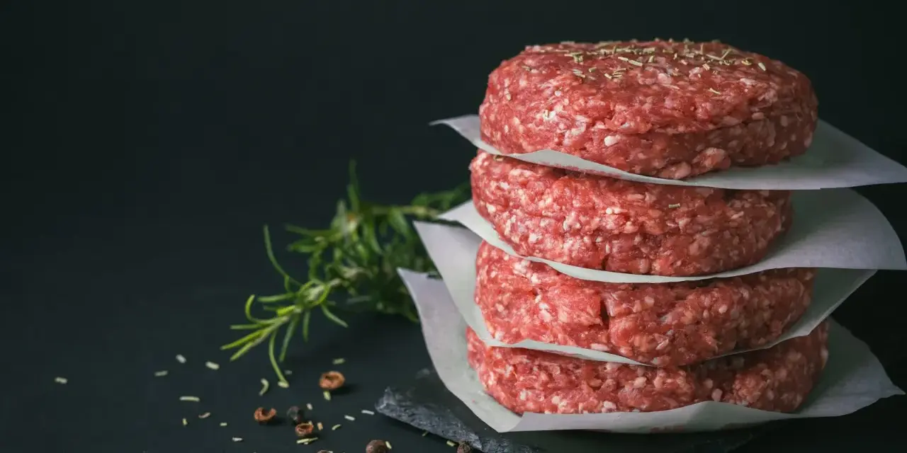 Stos świeżego, mielonego mięsa na burgery, przyprawionego ziołami i pieprzem, gotowe do grillowania.