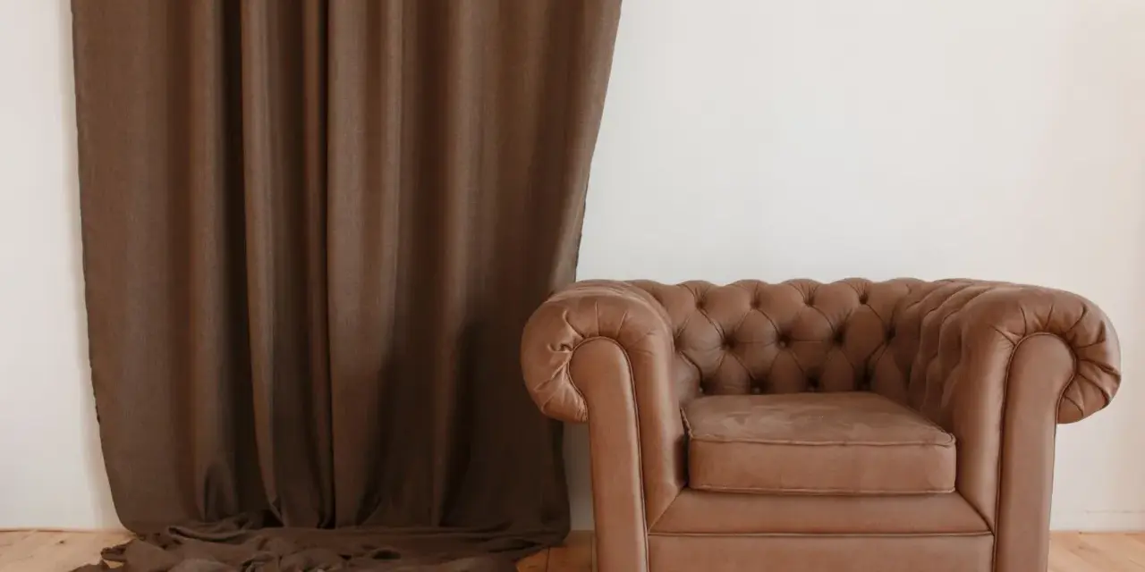 Butaca de cuero marrón estilo Chester junto a cortina marrón. ¿Cuánto cuesta tapizar una butaca como esta?