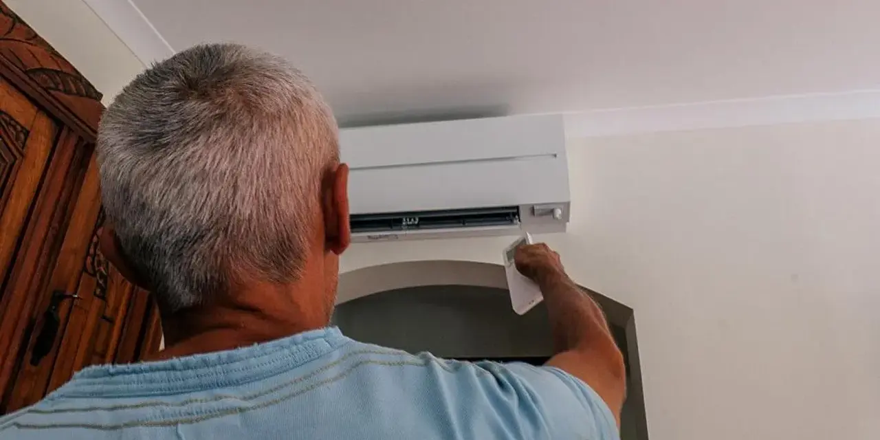 Uomo con telecomando regola il condizionatore per aria fredda, cercando sollievo dall'estate.