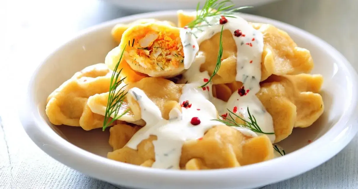 Pierogi z farszem, polane sosem, udekorowane koperkiem i pieprzem.